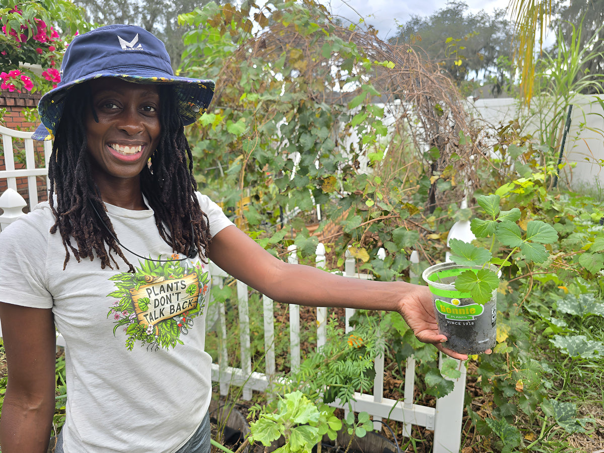 Toni Jefferson smiling and holding a strawberry plant in the garden